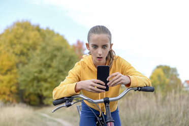 Porträt eines Mädchens, das sich an ein Fahrrad lehnt und auf ein Smartphone starrt - BFRF01948