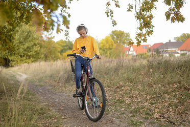 Mädchen mit Kopfhörern sitzt auf dem Fahrrad und schaut auf ihr Smartphone - BFRF01951