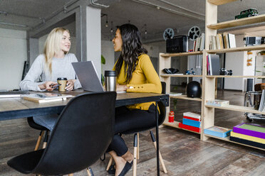 Two young businesswomen talking at conference table in loft office - GIOF05208