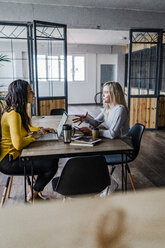 Zwei junge Geschäftsfrauen im Gespräch am Konferenztisch im Loftbüro - GIOF05210