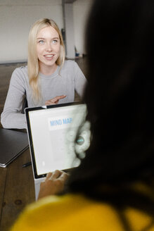 Zwei junge Geschäftsfrauen mit Laptop im Gespräch am Konferenztisch im Büro - GIOF05213