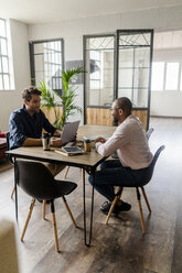Zwei junge Geschäftsleute unterhalten sich am Konferenztisch in einem Loftbüro - GIOF05214