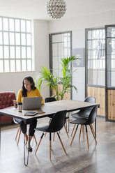 Young businesswoman sitting at desk in loft office using cell phone - GIOF05222