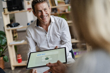 Smiling businessman holding tablet with a mind map during a presentation in loft office - GIOF05233