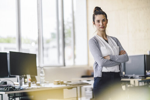 Porträt einer schönen jungen Frau, stehend im Büro, mit verschränkten Armen - RIBF00778