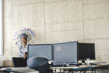 Young woman wearing Indian headdress, standing in office - RIBF00791