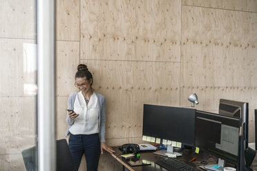 Junge Frau arbeitet im Büro, benutzt ein Smartphone, lacht - RIBF00794