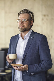 Geschäftsmann steht im Büro und trinkt Kaffee aus einer Holztasse - RIBF00802