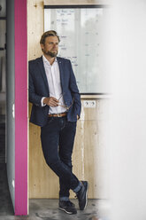 Geschäftsmann steht in einem Büro, hält eine Brille in der Hand und stützt sich auf eine weiße Tafel - RIBF00805