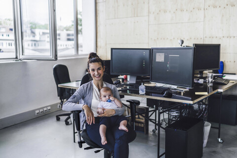 Arbeitende Mutter mit Baby auf dem Schoß, sitzend im Büro, lizenzfreies Stockfoto