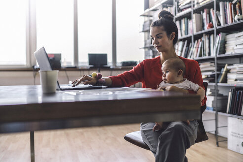 Arbeitende Mutter mit Baby auf dem Schoß, im Büro sitzend, mit Laptop - RIBF00824