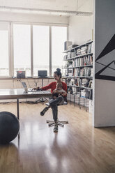 Working mother with baby on her lap, sitting in office, using laptop - RIBF00825