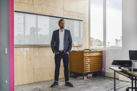 Geschäftsmann steht in seinem Büro vor einem Whiteboard, mit den Händen in den Taschen, lizenzfreies Stockfoto