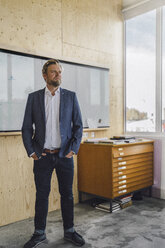 Businessman standing in his office in front of whiteboard, with hands in pockets - RIBF00849