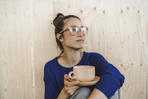 Junge Frau macht eine Pause im Büro und trinkt Kaffee aus einer Holztasse - RIBF00852