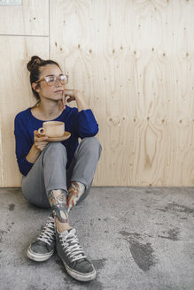 Junge Frau macht eine Pause im Büro und trinkt Kaffee aus einer Holztasse - RIBF00853