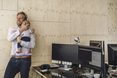 Ein berufstätiger Vater steht im Büro und hält seinen Sohn im Arm - RIBF00855
