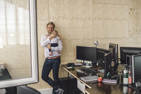 Ein berufstätiger Vater steht im Büro und hält seinen Sohn im Arm, lizenzfreies Stockfoto