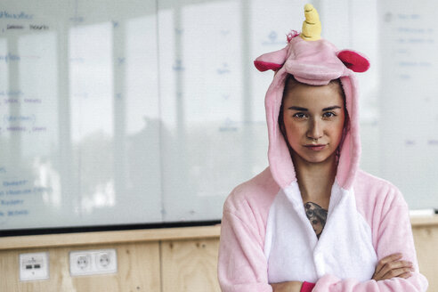 Woman wearing unicorn onesie, standing in front of whiteboard, looking stubborn - RIBF00860