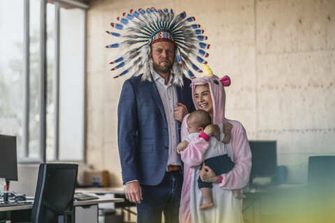 Man and woman, dressed as Indian and unicorn, standing in office, woman holding baby in her arms stock photo