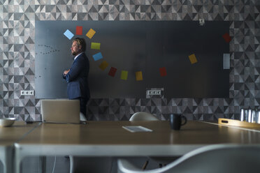 Businessman standing in front of magnet wall with a colorful headdress, made from sticky notes - RIBF00875