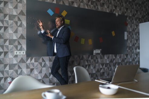 Businessman standing in front of magnet wall with a colorful headdress, made from sticky notes, roaring - RIBF00878