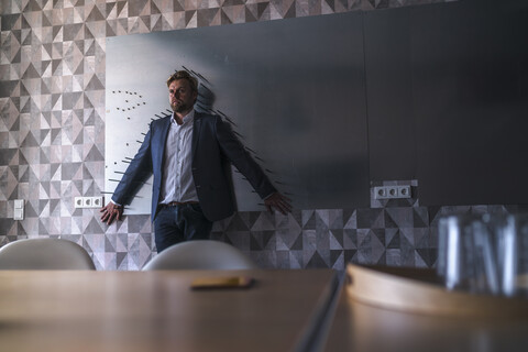 Geschäftsmann, der in einem Sitzungssaal mit dem Rücken zu einer Magnetwand steht, eingerahmt von Pfeilen, lizenzfreies Stockfoto