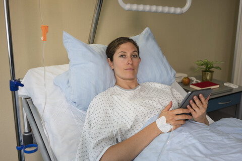 Porträt einer ernsthaften Patientin mit digitalem Tablet, die sich in einem Krankenhauszimmer ausruht und erholt, lizenzfreies Stockfoto