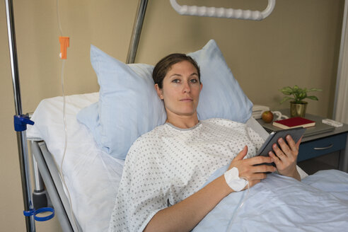 Portrait serious female patient with digital tablet, resting and recovering in hospital room - FSIF03420