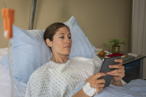 Female patient with digital tablet resting, recovering in hospital bed - FSIF03440