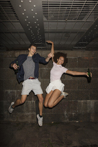 Porträt übermütiges junges Paar, das Bier trinkt und springt, lizenzfreies Stockfoto