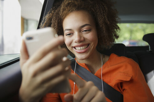 Lächelnde junge Frau, die ein Smartphone im Auto benutzt - FSIF03453