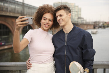 Junges Paar mit Smartphone nimmt Selfie auf Brücke - FSIF03454