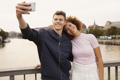 Affectionate young couple with smart phone taking selfie on urban bridge stock photo