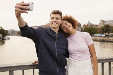 Affectionate young couple with smart phone taking selfie on urban bridge - FSIF03479