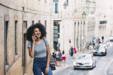 Smiling young woman talking on smart phone on urban street, Lisbon, Portugal - FSIF03512