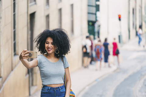 Junge Frau mit Smartphone nimmt Selfie auf städtischen Straße, lizenzfreies Stockfoto