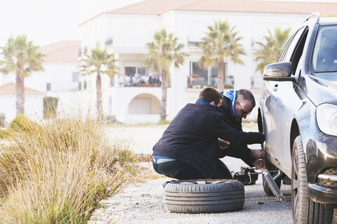 Vater und Sohn wechseln Autoreifen am Straßenrand, lizenzfreies Stockfoto