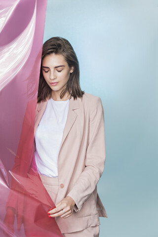 Porträt eines weiblichen Modemodells, das mit rosa Stoff posiert und nach unten schaut, lizenzfreies Stockfoto