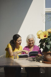 Ältere Mutter und Tochter lesen eine Zeitschrift auf einer sonnigen Terrasse - FSIF03558