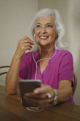 Lächelnde ältere Frau, die mit Kopfhörern und mp3-Player Musik hört - FSIF03570