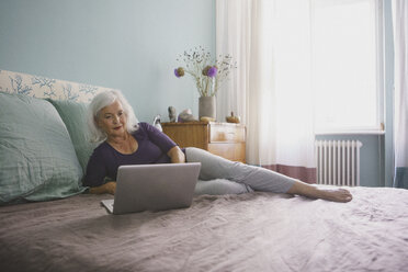 Ältere Frau mit Laptop auf dem Bett - FSIF03578