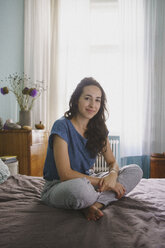 Porträt lächelnde Frau auf Bett sitzend - FSIF03580