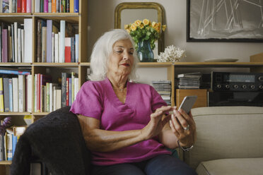 Ältere Frau benutzt ihr Smartphone auf dem Wohnzimmersofa - FSIF03599