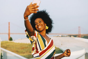 Selbstbewusste junge Frau, die ein Selfie mit ihrem Smartphone macht, mit der Brücke 25 de Abril im Hintergrund - FSIF03614