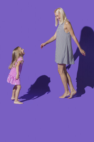 Sorglose Mutter und Tochter in gestreiften Kleidern tanzen vor lila Hintergrund, lizenzfreies Stockfoto