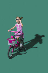 Mädchen mit Sonnenbrille Fahrradfahren gegen grünen Hintergrund - FSIF03657