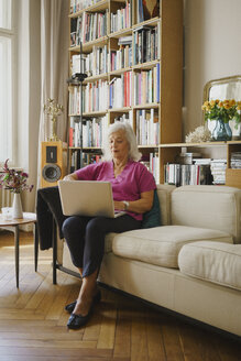 Senior woman using laptop on living room sofa - FSIF03691