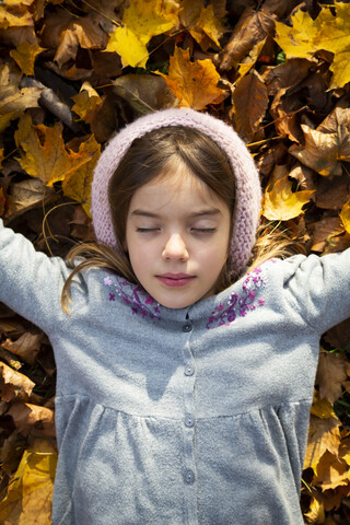 Porträt eines kleinen Mädchens, das auf Herbstblättern liegt, lizenzfreies Stockfoto