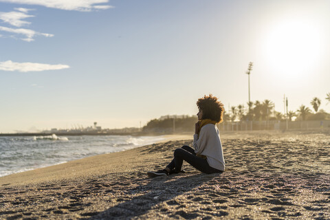 Frau sitzt bei Sonnenuntergang am Strand, lizenzfreies Stockfoto